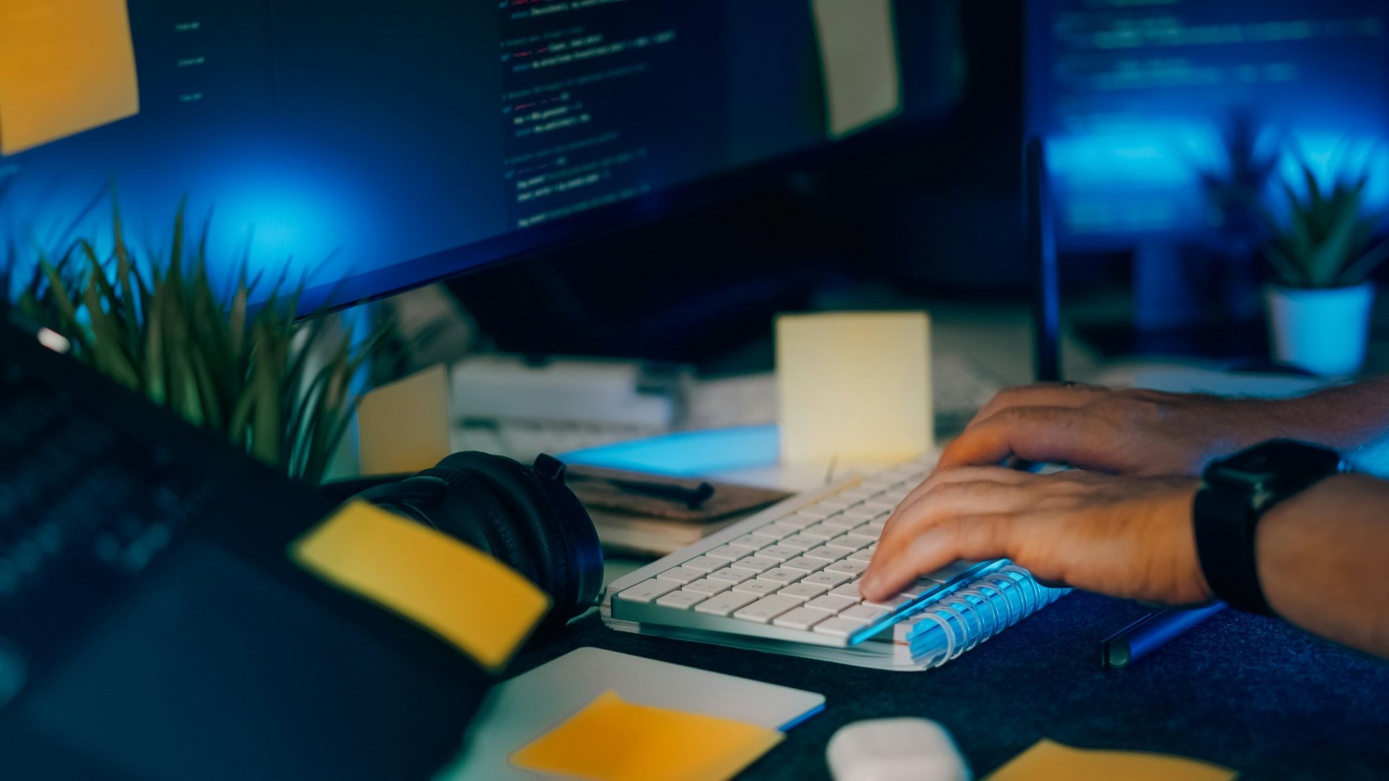Hands typing on a keyboard in front of screens with code